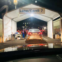 Vehicle at night below sign that reads "Lane 7/Carril 7" during drive-thru COVID-19 vaccination.
