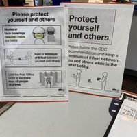 Image of signs in a post office that say please protect yourself and others. Masks or face coverings are required inside our lobby. Keep a minimum of six feet between yourself and others. Limit the Post Office lobby to no more than 10 people at a time.