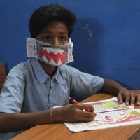 A hand colored mask resembling a shark made out of paper and worn by a child.