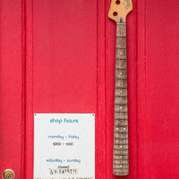 A red front door of Strange Guitarworks with a business hour sign and bass guitar neck.