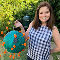 This is a picture taken of a women holding a representation of a COVID-19 germ she made, while standing in a backyard. 