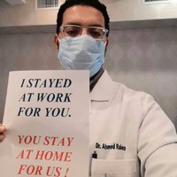 Image of a male doctor holding a sign which reads I stayed at work for you, you stay at home for us.