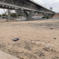 This is a picture of a face mask that has been discarded underneath a bridge in the dirt. 