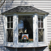Photograph of a house window that has a rabbit and a rainbow picture taped to it. 