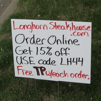 A hand written black and red sign telling about discount codes for a stake house