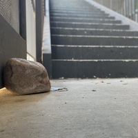 This is a picture of a discarded face mask resting partially behind a large rock on a concrete floor at the base of a stairwell