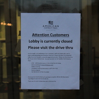 A sign from American Community Bank that says 
"Attention Customers. Lobby is currently closed. Please visit the drive thru. For the health and well-being of our customers, staff and community, and to meet social distancing best practices, American Community Bank has closed all lobby hours to the public, except by appointment only. Please visit the drive thru for all teller transactions. Account services can be handled the follow ways: ATM-ACB locations and all 7/11 ATMs free of charge, online banking at www.ACBalways.com, mobile banking, telephone banking automated at 877-244-7222, remote deposit, call the branch at 516-742-4300. American Community Bank will continue to monitor all new developments regarding the Coronavirus (Covid-19). Thank you for your cooperation and understanding." 