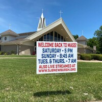 A church yard sign reading "Welcome Back to Mass!" along with the service schedule and an online link to a livestream. 