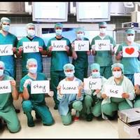 Image of doctors wearing masks holding signs that say we stay here for you please stay home for us.