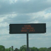 Highway sign with text saying, "SOCIAL DISTANCING SAVES LIVES"