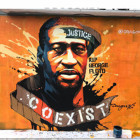 This is a picture taken of a mural painted in memory of George Floyd. A banner on the top reads 'Justice', next to a caption reading 'RIP George Floyd". A second banner below the image reads "Coexist". 