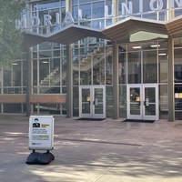 This is a picture taken outside the ASU Memorial Union. A sign that has been put up in front reading: "Everyone is required to wear a face covering while in ASU buildings. If you are fully vaccinated, outside, and not in a crowd, a face covering is optional." 