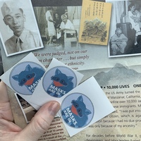 This is a picture taken of stickers promoting the wearing of masks. A program relating to Manzanar Internment Camp sits below it. 