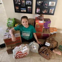 Young girl sits in front of boxes of Girl Scouts cookies on the floor.