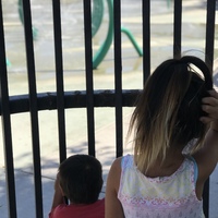 Two children looking at a closed playground through a gate.