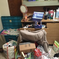 This is a picture taken of someone's messy dresser area. Multiple bags of other objects are scattered on the floor in front of the dresser. 